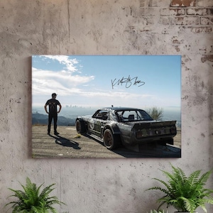 May include: A rectangular wall art print featuring a dark, wide-body custom car parked on a hilltop overlooking a distant city skyline. A figure stands beside the vehicle, and a black handwritten signature is visible in the upper sky area.
