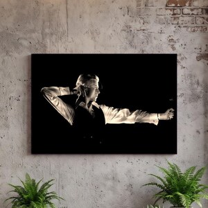 May include: A rectangular wall art print featuring a high-contrast black and white photograph of a person in a light-colored long-sleeved shirt and dark vest, posed with one arm raised behind the head and the other extended forward.