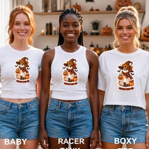 May include: Three white tops paired with blue denim shorts. Each top features a graphic of a ghost wearing a plaid hat and scarf, holding a pumpkin, with the text "BASICALLY BASIC BOO" underneath. The tops are a baby tee, a racer tank, and a boxy tee.