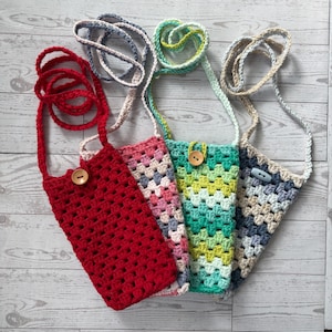 May include: Four colorful crochet phone pouches with long straps. The pouches are red, pink, green, and blue, each with a unique pattern and wooden button closure. The straps are in matching or complementary colors.
