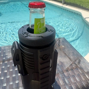 Pode incluir: Um refrigerador de bebidas cil&iacute;ndrico preto com um exterior texturizado de estilo t&aacute;tico, apresentando trilhos verticais e um abridor de garrafas lateral. Uma garrafa de vidro com tampa vermelha e r&oacute;tulo verde Smirnoff ICE est&aacute; inserida.