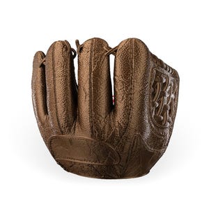 Puede incluir: Un guante de b&eacute;isbol de color bronce met&aacute;lico con una superficie texturizada, secciones de dedos cosidas y un patr&oacute;n de red tejido en el lateral. El guante tiene un dise&ntilde;o estructurado con costuras visibles y detalles de cordones.
