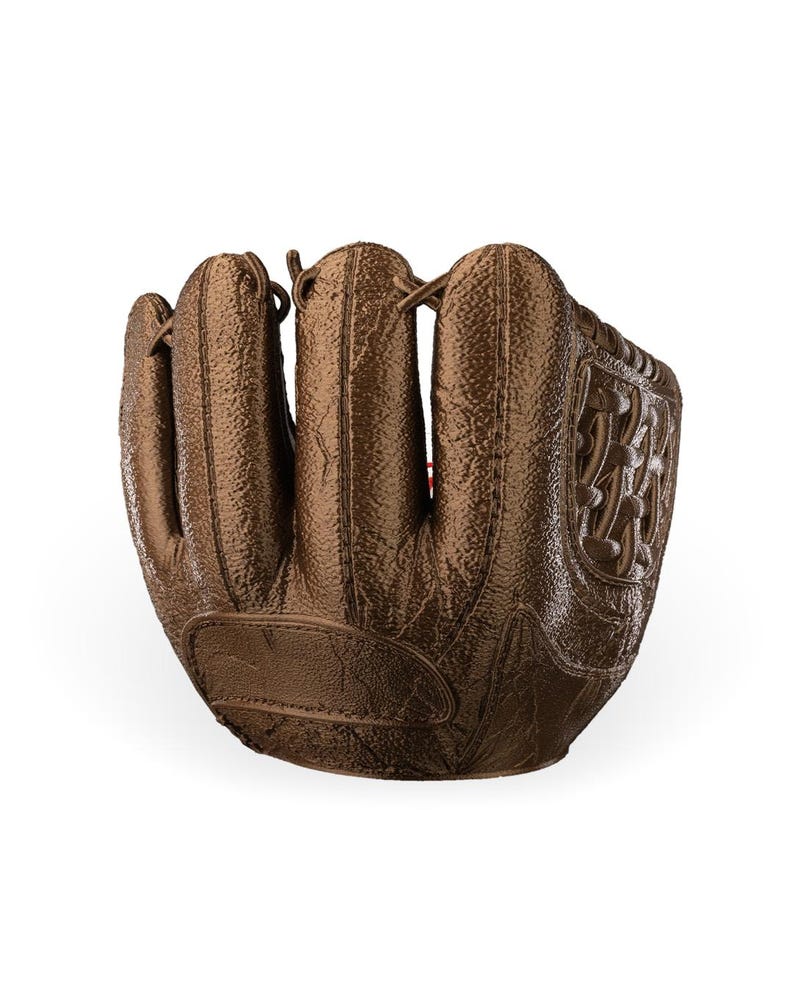 Puede incluir: Un guante de b&eacute;isbol de color bronce met&aacute;lico con una superficie texturizada, secciones de dedos cosidas y un patr&oacute;n de red tejido en el lateral. El guante tiene un dise&ntilde;o estructurado con costuras visibles y detalles de cordones.