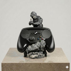 Puede incluir: Un mando de videojuegos negro apoyado sobre una base gris texturizada que simula una roca. Detr&aacute;s del mando, una figura gris esculpida de un soldado con equipo t&aacute;ctico sostiene un arma de fuego. El mando cuenta con una cruceta, dos paneles t&aacute;ctiles circulares, un bot&oacute;n central con el logo de Steam y cuatro botones de acci&oacute;n de colores etiquetados como A, B, X e Y.
