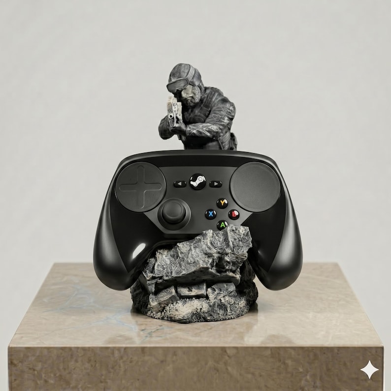 Puede incluir: Un mando de videojuegos negro apoyado sobre una base gris texturizada que simula una roca. Detr&aacute;s del mando, una figura gris esculpida de un soldado con equipo t&aacute;ctico sostiene un arma de fuego. El mando cuenta con una cruceta, dos paneles t&aacute;ctiles circulares, un bot&oacute;n central con el logo de Steam y cuatro botones de acci&oacute;n de colores etiquetados como A, B, X e Y.