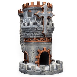 May include: A gray and copper-colored castle-shaped dice tower featuring a prominent cross emblem on the upper turret, crenelated battlements, a central arched doorway, and a side window, all rendered with a textured stone-like finish.