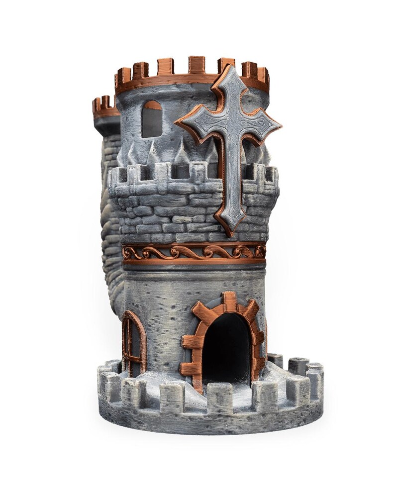 May include: A gray and copper-colored castle-shaped dice tower featuring a prominent cross emblem on the upper turret, crenelated battlements, a central arched doorway, and a side window, all rendered with a textured stone-like finish.