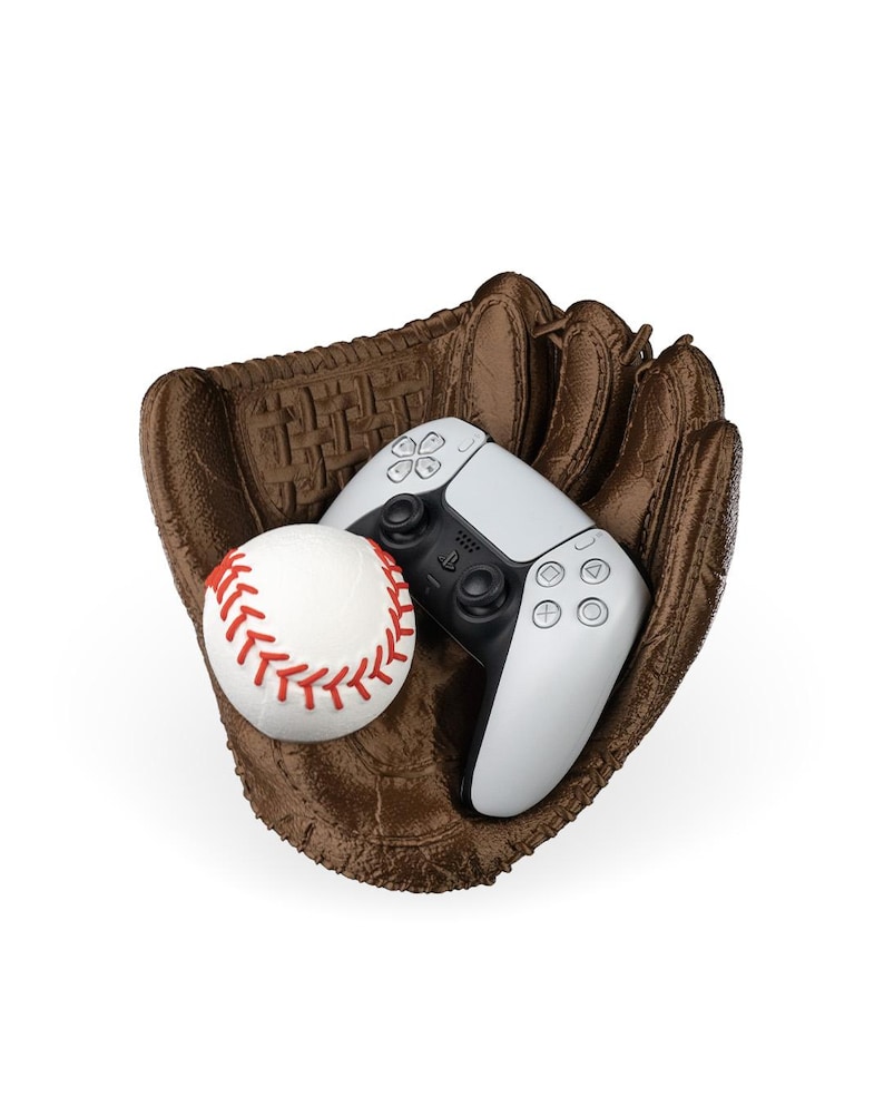 Puede incluir: Un guante de b&eacute;isbol marr&oacute;n texturizado que sostiene una pelota de b&eacute;isbol blanca con costuras rojas y un mando de videojuego inal&aacute;mbrico blanco y negro. El mando cuenta con una cruceta, dos joysticks anal&oacute;gicos y cuatro botones de acci&oacute;n.