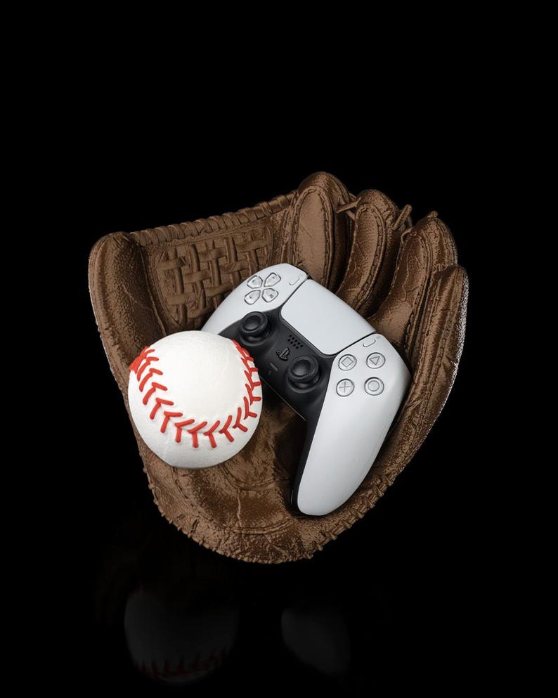 Puede incluir: Un guante de b&eacute;isbol de cuero marr&oacute;n que sostiene una pelota de b&eacute;isbol blanca con costuras rojas y un mando de videojuego inal&aacute;mbrico blanco y negro con el logotipo de PlayStation y s&iacute;mbolos geom&eacute;tricos ic&oacute;nicos sobre fondo negro.