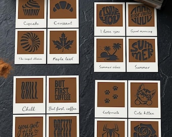 Può includere: Una collezione di sedici cartoline quadrate con bordi bianchi e centri marroni, ognuna caratterizzata da un design nero ritagliato unico e un'etichetta scritta a mano. I disegni includono un cupcake, un croissant, un bagel, una foglia d'acero, frasi sul caffè, motivi estivi, un gattino, un ragno e una rosa.