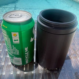 以下が含まれることがあります： 銀色のプルタブと白い文字でRecycle Meと書かれた緑色のアルミ製スプライト缶の隣に、ネジ山のある上部リムを備えたマットブラックの円筒形ドリンククーラーが置かれており、どちらも濃い茶色の編み込み模様の表面に直立しています。