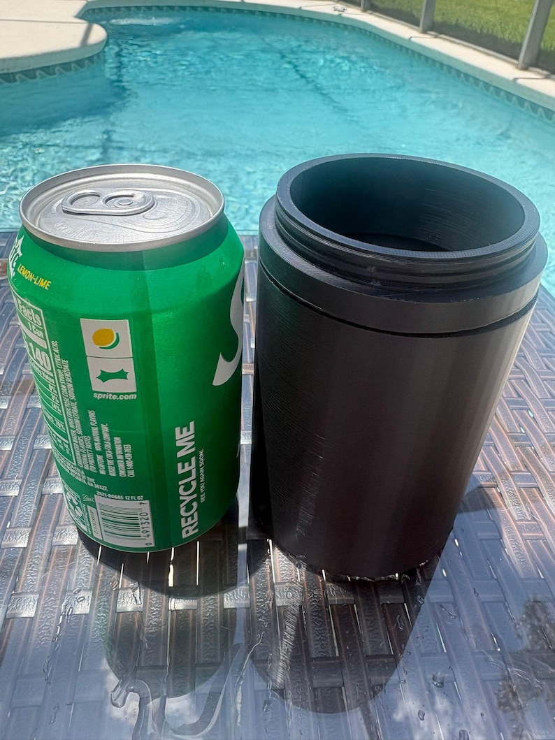 以下が含まれることがあります： 銀色のプルタブと白い文字でRecycle Meと書かれた緑色のアルミ製スプライト缶の隣に、ネジ山のある上部リムを備えたマットブラックの円筒形ドリンククーラーが置かれており、どちらも濃い茶色の編み込み模様の表面に直立しています。