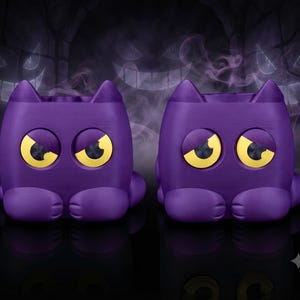May include: Two purple, cat-shaped containers with pointed ears and large, yellow, expressive eyes. Each container features a smooth, matte finish and a rounded body with visible paw details at the base, designed with a hollow top opening.