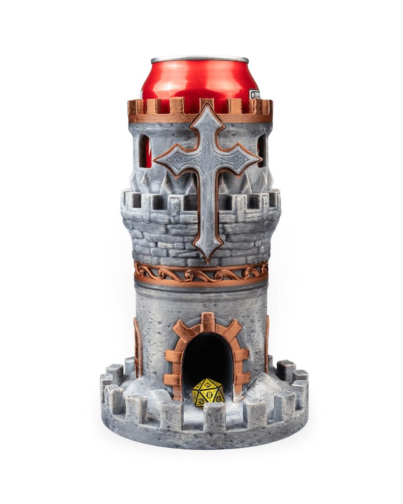 May include: A gray and copper-colored castle-shaped dice tower with a crenelated top and base. The structure features a prominent cross emblem on the front and a central arched doorway containing a single yellow twenty-sided die. A red can is inserted.