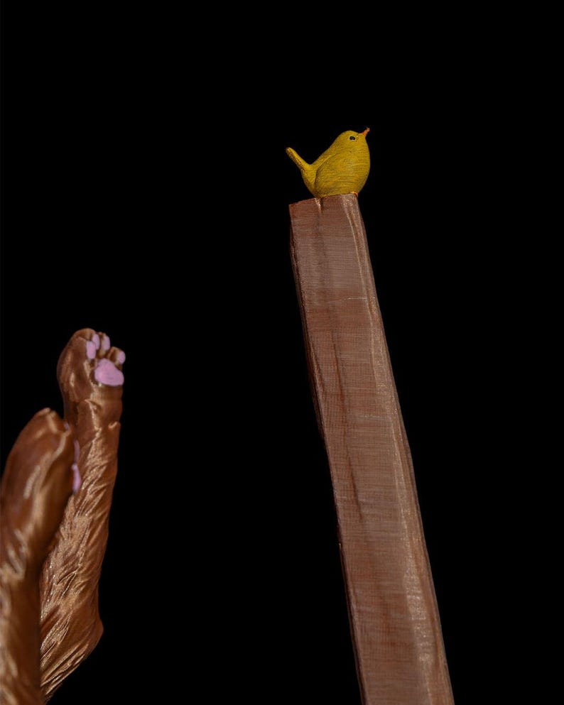 May include: A small yellow bird perched on top of a tall, rectangular brown wooden post. To the left, a pair of brown animal paws with light pink paw pads are visible, showing textured fur details and distinct toes against a black background.