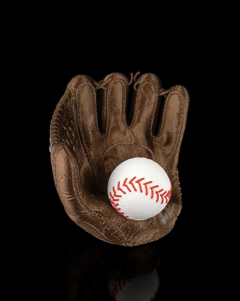 Puede incluir: Un guante de b&eacute;isbol marr&oacute;n con superficie texturizada que sostiene una pelota de b&eacute;isbol blanca con costuras rojas prominentes. El guante tiene compartimentos para los dedos y un dise&ntilde;o de red, sobre un fondo negro con un sutil reflejo.