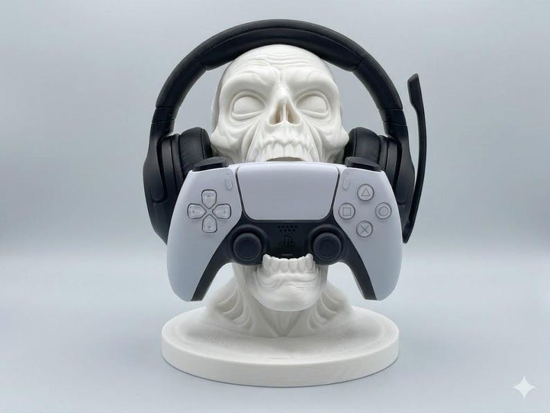 May include: A white skull-shaped stand holds a pair of black over-ear gaming headphones with a microphone boom and a white and black wireless video game controller. The skull rests on a circular base, providing a display for gaming accessories.