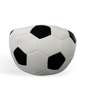 Op de afbeelding: Een pluche, bolvormig kussen in de vorm van een voetbal met het klassieke zwart-witte patroon van vijfhoeken en zeshoeken. Het oppervlak heeft een zachte, stofachtige textuur met zichtbare stiksels langs de naden van elk paneel.