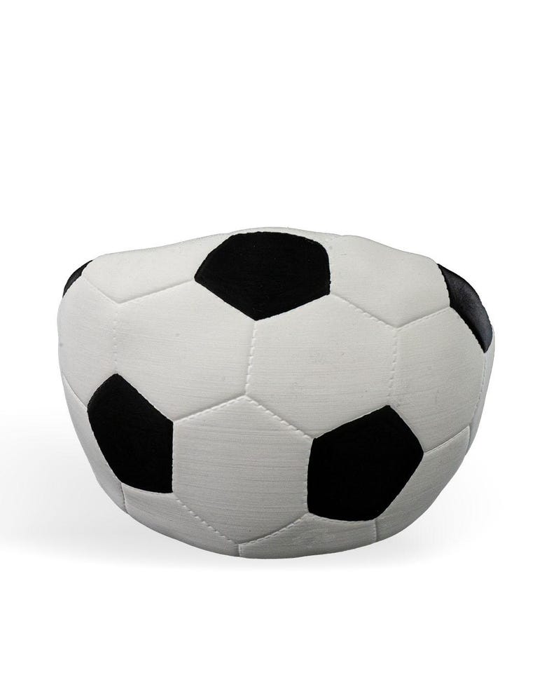 Op de afbeelding: Een pluche, bolvormig kussen in de vorm van een voetbal met het klassieke zwart-witte patroon van vijfhoeken en zeshoeken. Het oppervlak heeft een zachte, stofachtige textuur met zichtbare stiksels langs de naden van elk paneel.