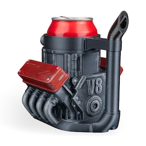 May include: A black and red V8 engine-shaped beverage can holder featuring a prominent exhaust pipe handle. The structure is molded with detailed engine components, including red valve covers and the text V8 embossed on the side, designed to securely hold a standard red aluminum drink can.