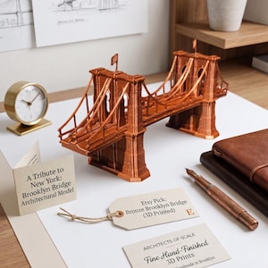 Peut inclure: Un modèle architectural imprimé en 3D de couleur cuivre représentant le pont de Brooklyn. Le modèle présente des câbles de suspension et des tours détaillés. Des cartes accompagnantes affichent le texte A Tribute to New York: Brooklyn Bridge Architectural Model, Etsy Pick: Bronze Brooklyn Bridge (3D Printed), et ARCHITECTS OF SCALE Fine Hand-Finished 3D Prints Est. 2023 | Handmade in Brooklyn.