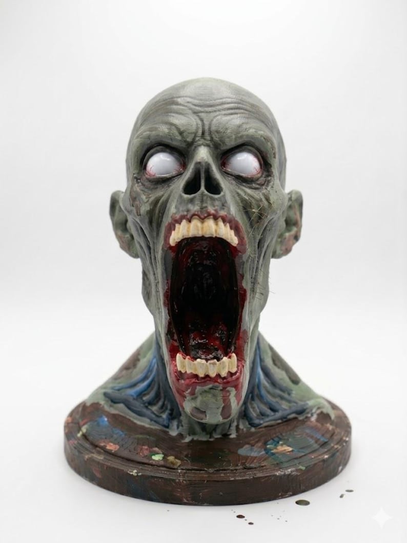 May include: A sculpted bust of a humanoid creature with grey skin, a wide-open mouth revealing dark red interior details, and white, pupil-less eyes. The figure features prominent facial muscles, visible teeth, and sits on a circular base.