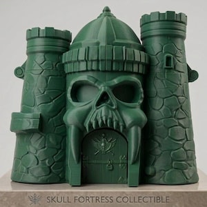 Op de afbeelding: Een donkergroen plastic schedelvesting verzamelobject met twee zijtorens met steenachtige texturen en een centrale structuur in de vorm van een schedel met een poort. De basis toont de tekst SKULL FORTRESS COLLECTIBLE.