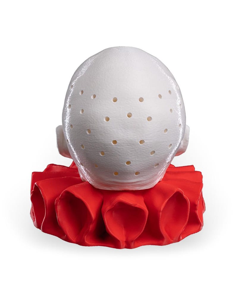 May include: A white, rounded, dome-shaped object featuring a textured surface with numerous small, evenly spaced circular perforations. The object is positioned atop a vibrant, solid red, pleated, circular collar-like base with deep folds.