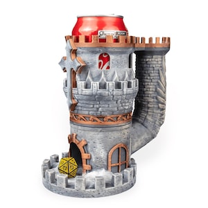 May include: A gray stone-textured castle dice tower with copper-colored accents, featuring a crenelated top, a cross emblem, and an arched doorway. A yellow twenty-sided die sits at the base, and a red beverage can is inserted into the top opening.