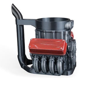 May include: A black mug shaped like a V8 engine block with a tall exhaust pipe handle. The design features a prominent red valve cover with visible screw details and metallic silver exhaust headers extending from the side of the engine block structure.