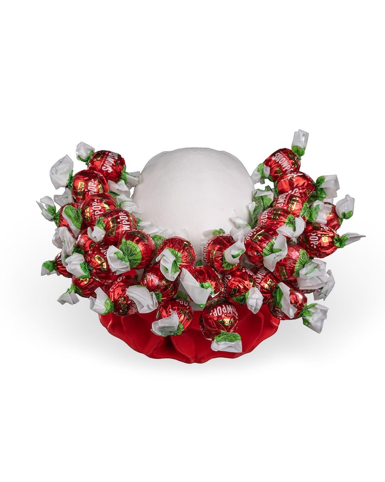 May include: A white foam sphere base adorned with numerous red foil-wrapped sweets, each featuring white twisted ends and the text "SHOWPOP" printed in white. The sweets are arranged in a dense cluster around the centre of the sphere.