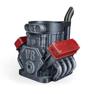 May include: A dark gray mug shaped like a V8 engine block with red valve covers and a black exhaust pipe extending from the back. The front of the engine block features the embossed text V8, along with detailed mechanical components and pipes.