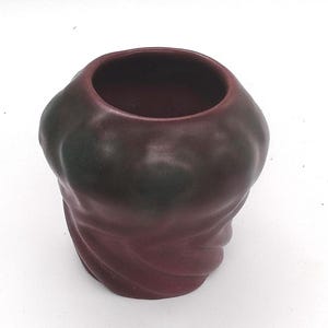 May include: A small, rounded ceramic vessel with a deep burgundy matte finish and subtle dark charcoal shading. The exterior features a distinct, swirling, organic texture that tapers toward the base, topped with a wide, circular opening.