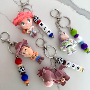 Op de afbeelding: Vier sleutelhangers met figuren van een cowgirl, een space ranger, een cowboy en een paard. Elke sleutelhanger heeft een metalen ring, een sluiting en gekleurde siliconen kralen. Twee sleutelhangers bevatten witte letterkralen die NLP en ARG spellen.
