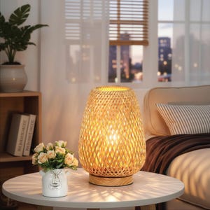 May include: A table lamp with a woven bamboo shade in a tapered cylindrical shape, featuring a light wood base. The lamp emits a warm, glowing light through the intricate lattice pattern of the bamboo, casting soft shadows on the surface below.
