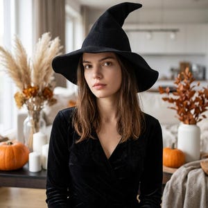 May include: A black felt witch hat with a wide, slightly curved brim and a pointed, structured crown. The hat features a smooth, matte texture and a classic conical shape, designed to sit securely on the head with a deep, rounded interior.