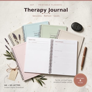 May include: A collection of spiral-bound therapy journals in pastel colors including blue, green, and pink. The open journal displays lined pages with headers for Session Notes and Coping Strategies. Includes a brown pen and a black stone.