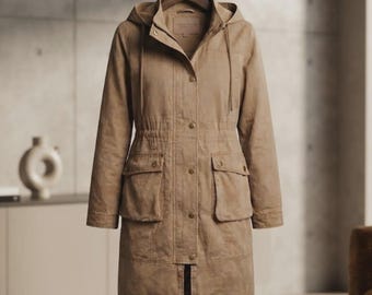 Könnte beinhalten: Eine beigefarbene Utility-Jacke mit Kapuze, Knopfleiste auf der Vorderseite, langen Ärmeln und zwei großen Pattentaschen an der Taille. Die Jacke verfügt über eine Kapuze mit Kordelzug und eine taillierte Passform, hängend an einem Holzkleiderbügel.