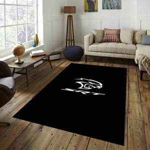 Può includere: Un tappeto rettangolare con sfondo nero a tinta unita, caratterizzato da una grande grafica bianca di un logo stilizzato a forma di testa di gatto posizionato sopra la scritta SRT in un carattere grassetto e pulito.
