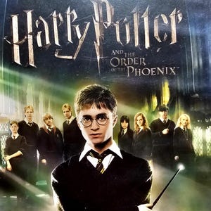 Puede incluir: Una caja de videojuego de PlayStation para Harry Potter y la Orden del Fénix. La portada presenta un retrato central de Harry Potter sosteniendo una varita, rodeado de otros personajes con uniformes escolares sobre un fondo gótico oscuro.