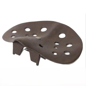 Puede incluir: Un asiento de tractor de metal marrón oxidado con forma redondeada y múltiples agujeros. El asiento tiene dos soportes metálicos en la parte inferior.