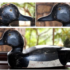 May include: A black and white wooden duck decoy with a white stripe across the chest. The decoy has a black painted finish and realistic details, including a painted eye.