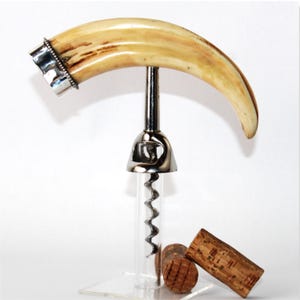 May include: A distinctive wine opener with a curved, ivory-coloured tusk handle and a silver-coloured metal accent. The opener has a clear glass tube with a corkscrew and is displayed with two corks.