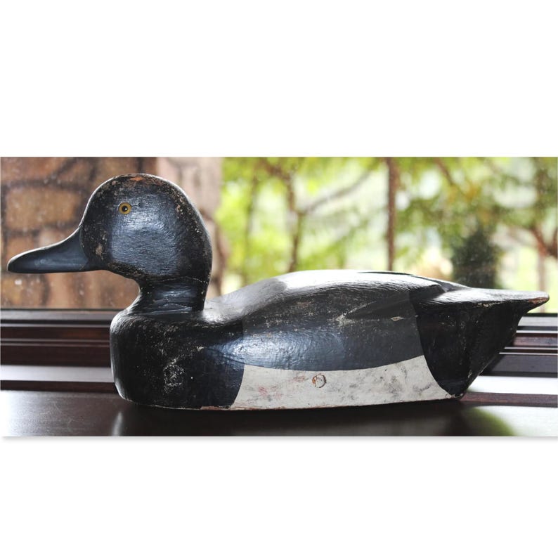 May include: A black and white wooden duck decoy with a yellow eye. The decoy is painted with black and white paint and has a white stripe on its belly.