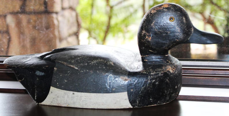 May include: A black and white wooden duck decoy with a white stripe around the middle. The decoy has a black eye with a yellow iris.