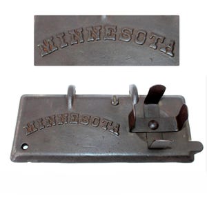 May include: A cast iron stove door with the word "MINNESOTA" embossed on it. The door has two metal hooks and a metal latch.