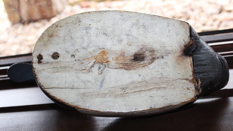May include: A wooden duck decoy with a white painted body and a black head. The decoy has a weathered appearance and shows signs of age.