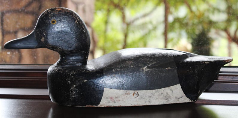May include: A black and white wooden duck decoy with a white stripe across the chest. The decoy has a black eye and a realistic shape.