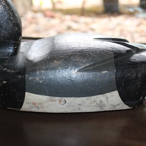 May include: A black and white wooden duck decoy with a gray painted body and a white painted stripe around the middle. The decoy has a black painted head and beak.