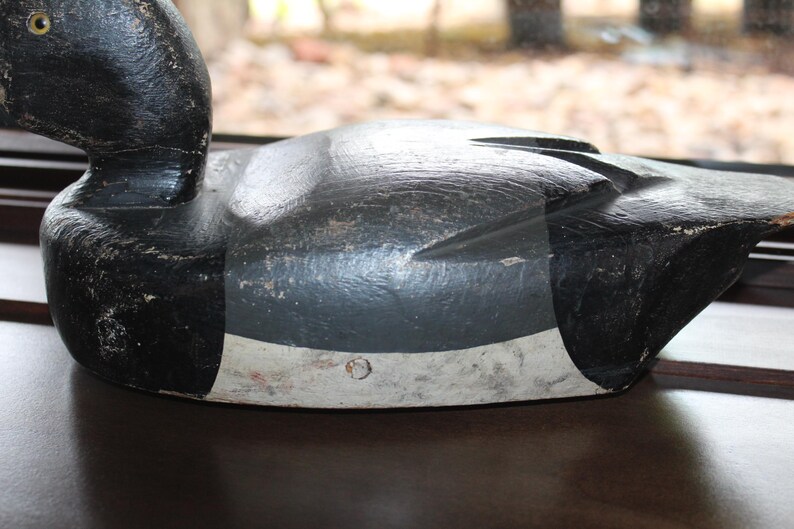 May include: A black and white wooden duck decoy with a gray painted body and a white painted stripe around the middle. The decoy has a black painted head and beak.